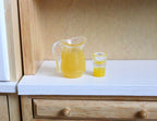 1:12 scale miniature orange juice pitcher and glass, set of 2, clear with orange juice, shown on a kitchen counter