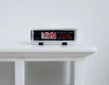 1:12 scale miniature digital alarm clock radio in black with red display digits and silver trim, on a white table