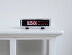 1:12 scale miniature digital alarm clock radio in black with red display digits and silver trim, on a white table