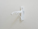 1:12 scale miniature white metal scroll wall bracket with hook arm, shown mounted on a white wall