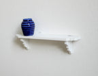 1:12 scale miniature wood wall shelf in white with scroll brackets, shown mounted with a blue vase on top