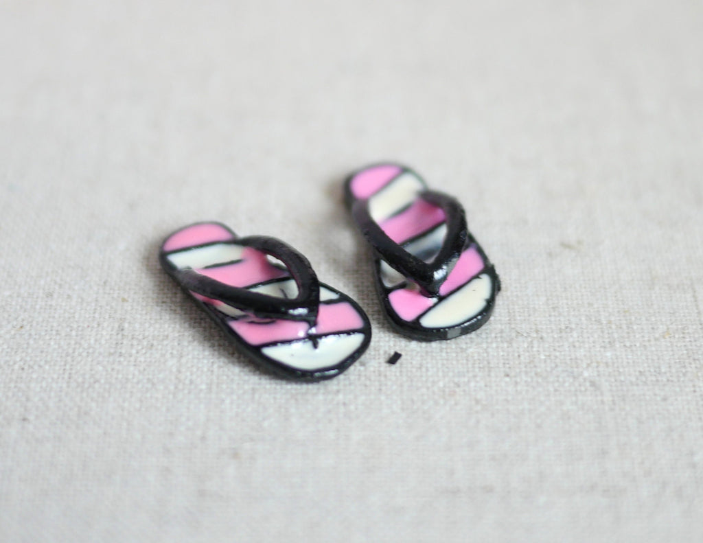 1:12 scale miniature metal flip flops in black and pink with white stripes, pair, shown on a linen surface