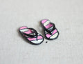 1:12 scale miniature metal flip flops in black and pink with white stripes, pair, shown on a linen surface