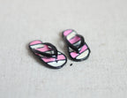 1:12 scale miniature metal flip flops in black and pink with white stripes, pair, shown on a linen surface