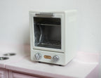 1:12 scale miniature toaster oven in light gray with clear door, rack, tray and two dials, on a white counter