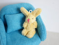 1:12 scale miniature long hair plush bunny doll in yellow, sitting, with pink nose, shown on a blue sofa