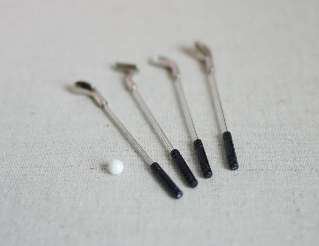 1:12 scale miniature golf clubs with ball, set of 5, silver clubs with black grips and a white ball, on linen