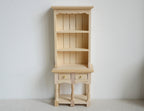 1:12 scale miniature unpainted wood narrow bookshelf cabinet with 3 shelves, two drawers and open base, against a white wall