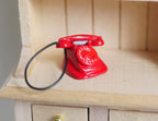 1:12 scale miniature metal rotary dial telephone in red with black coiled cord, shown on a wood hutch shelf