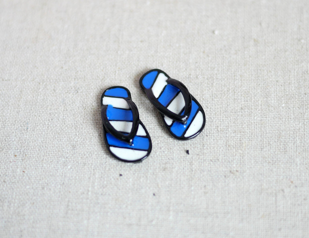 1:12 scale miniature metal striped flip flops in navy and white, one pair with black straps, on a light gray surface
