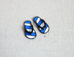 1:12 scale miniature metal striped flip flops in navy and white, one pair with black straps, on a light gray surface
