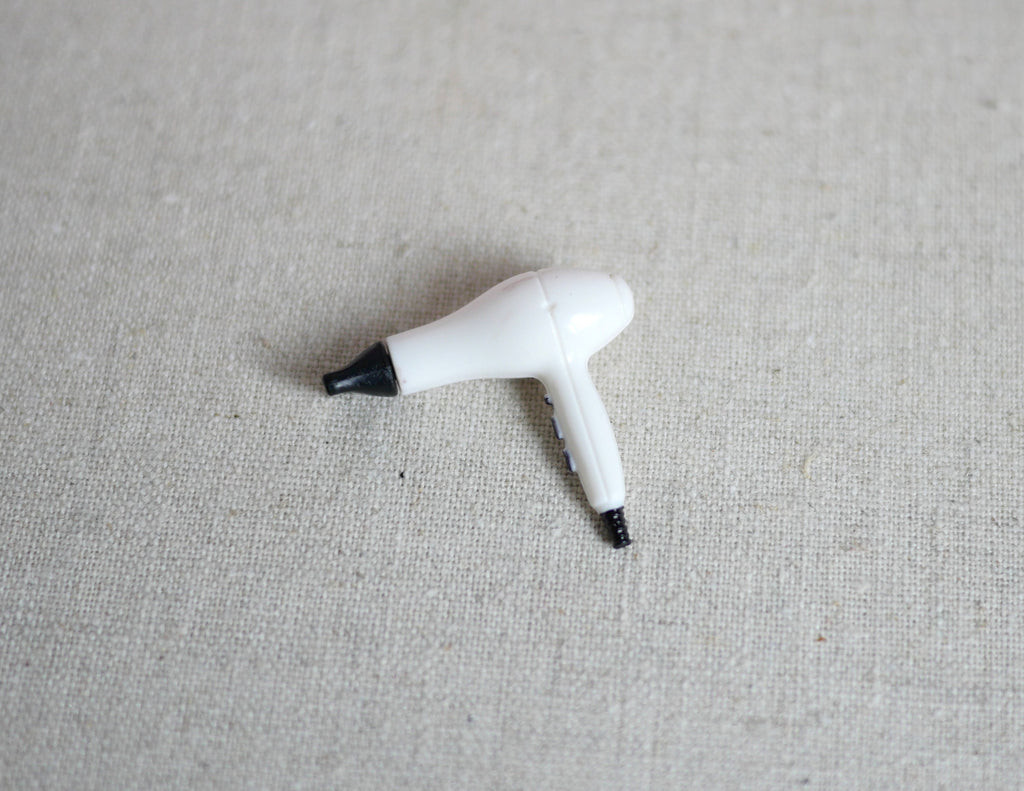 1:12 scale miniature hair dryer in white and black with cord, shown on a beige linen surface