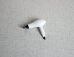 1:12 scale miniature hair dryer in white and black with cord, shown on a beige linen surface