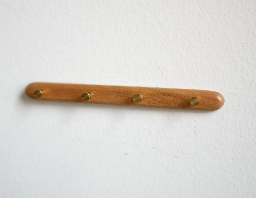 1:12 scale miniature wood wall coat rack in brown with 4 brass tone pegs, shown mounted on a white wall