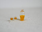 1:12 scale miniature whiskey decanter with gold stopper and 2 glasses, set of 3, filled with amber liquid, on a white surface