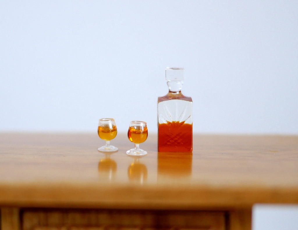 1:12 scale miniature whiskey decanter with stopper and 2 glasses, set of 3, dark amber filled, shown on a wood table