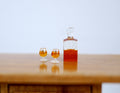 1:12 scale miniature whiskey decanter with stopper and 2 glasses, set of 3, dark amber filled, shown on a wood table