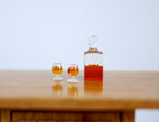 1:12 scale miniature whiskey decanter with stopper and 2 glasses, set of 3, dark amber filled, shown on a wood table