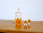 1:12 scale miniature round faceted whiskey decanter with 2 glasses, set of 3, amber filled, on a wood table