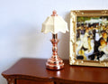 1:12 scale miniature table lamp with copper base and cream pleated shade, non-electric, beside a gold framed painting