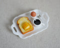 1:12 scale miniature breakfast tray with buttered toast, boiled egg and black coffee, white tray on linen fabric