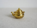 1:12 scale miniature gold metal kettle with lid and swing handle, round body, shown on a light gray surface