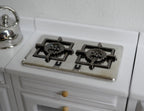 1:12 scale miniature metal 2 burner cooktop with black grates, silver finish, shown on a white kitchen counter