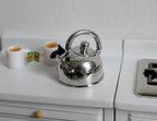 1:12 scale miniature metal water boiler kettle in silver with lid and looped handle, shown on a white kitchen counter