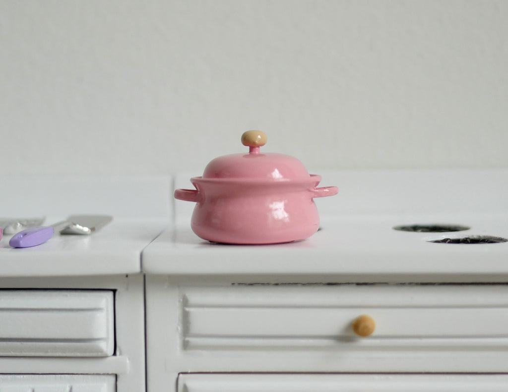 1:12 scale miniature pink metal cooking pot with lid, 2 side handles and a wood knob, shown on a white kitchen counter