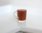 1:12 scale miniature clear mug of hot chocolate with a handle, brown drink, shown on a white counter