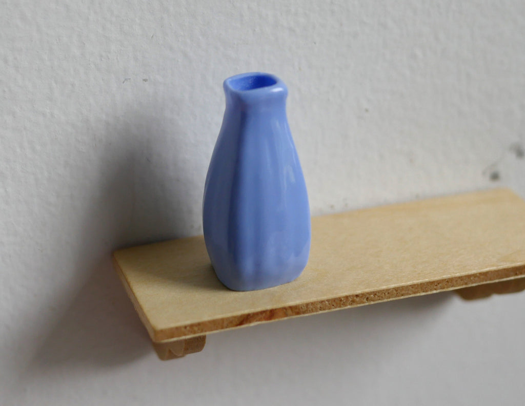 1:12 scale miniature ribbed vase in periwinkle blue with a narrow neck, shown on a small wood shelf
