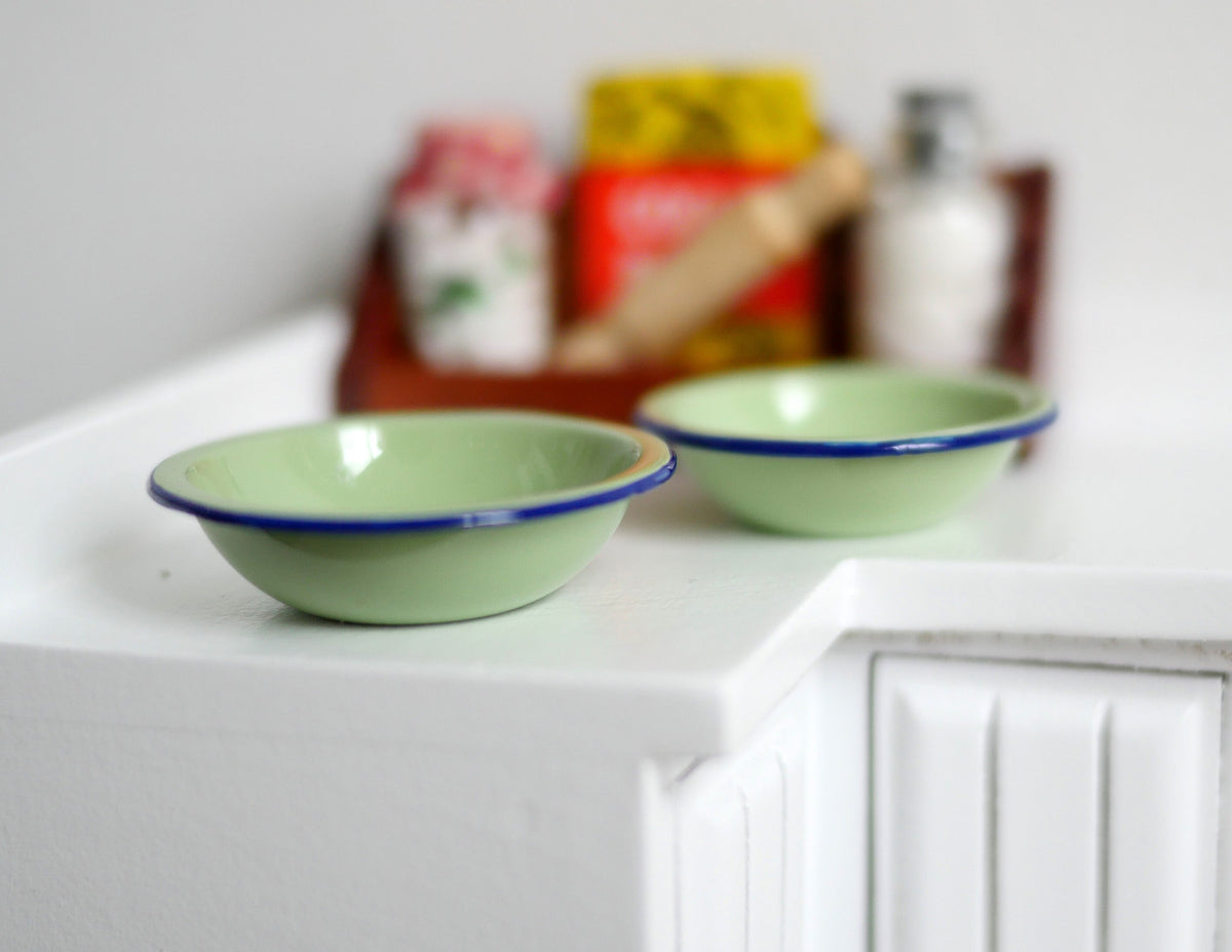1:12 scale miniature enamelware style bowls in sage green with navy rims, set of 2, large and small, on a white counter