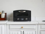 1:12 scale miniature toaster oven in black with clear door, rack and tray, shown on a white kitchen cabinet
