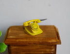 1:12 scale miniature metal rotary dial telephone in yellow, shown on a wood side table