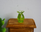 1:12 scale miniature translucent ruffled vase in green with ribbed body, shown on a wood side table