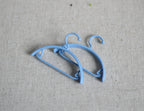 1:12 scale miniature clothes hangers in light blue, set of 2, shown lying on a beige fabric surface