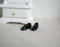 1:12 scale miniature men's dress shoes in glossy black, pair, shown on a floor beside a white dresser