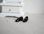 1:12 scale miniature men's dress shoes in glossy black, pair, shown on a floor beside a white dresser