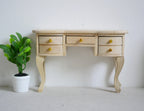 1:12 scale miniature unpainted wood vanity desk with drawers and cabriole legs, shown beside a small potted plant
