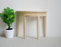 1:12 scale miniature unpainted wood half moon table with 3 legs, shown against a wall beside a potted plant