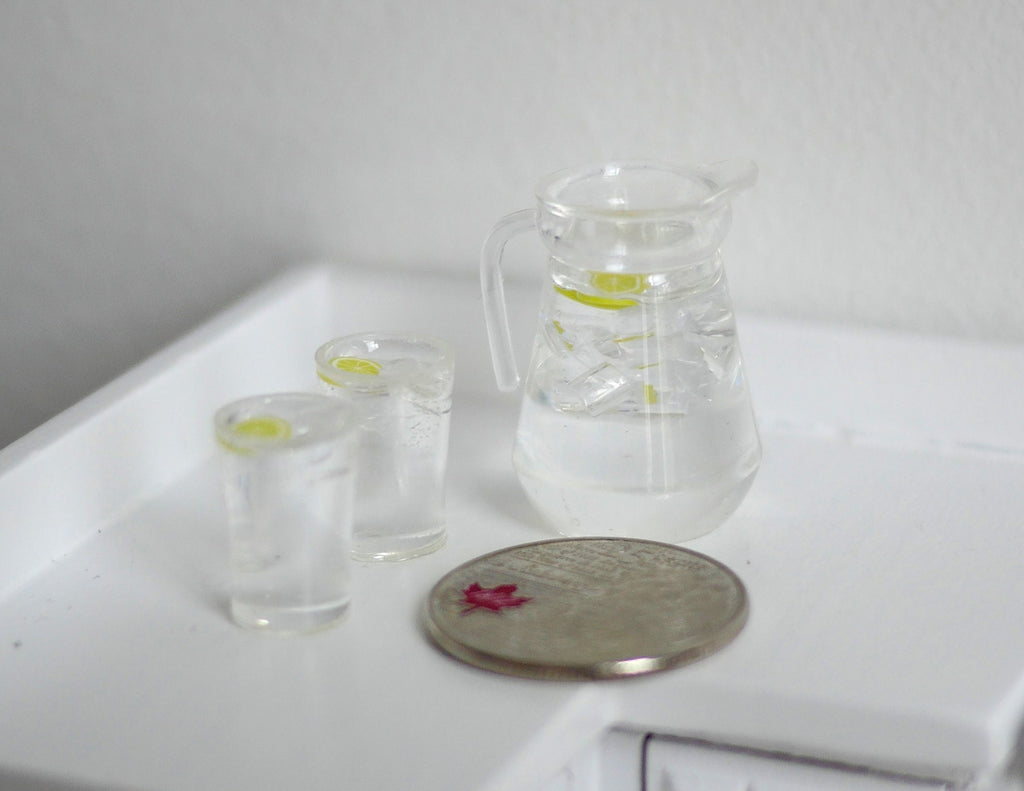 1:12 scale miniature lemon water dispenser with ice and 2 glasses, set of 3, clear, on a white counter beside a coin
