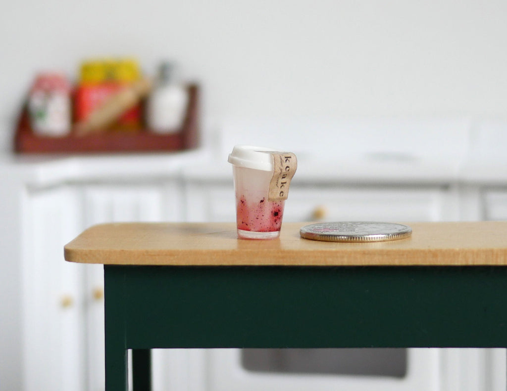 1:12 scale miniature smoothie cup in pink with a lid, shown on a kitchen table beside a coin for scale