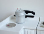 1:12 scale miniature pressure cooker with lid in silver with black handle, shown on a white counter beside a coin