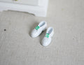 1:12 scale miniature men's white sneakers with green stripes, 1 pair, shown on a beige fabric surface