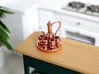 1:12 scale miniature metal teapot, glasses and tray set in shiny copper, 6 pieces, shown on a kitchen island