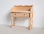 1:12 scale miniature unpainted wood writing desk with gallery rail, 1 drawer and turned legs, against a white wall