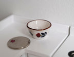 1:12 scale miniature ceramic bowl with fruit pattern and red rim on white, on a counter beside a coin for scale
