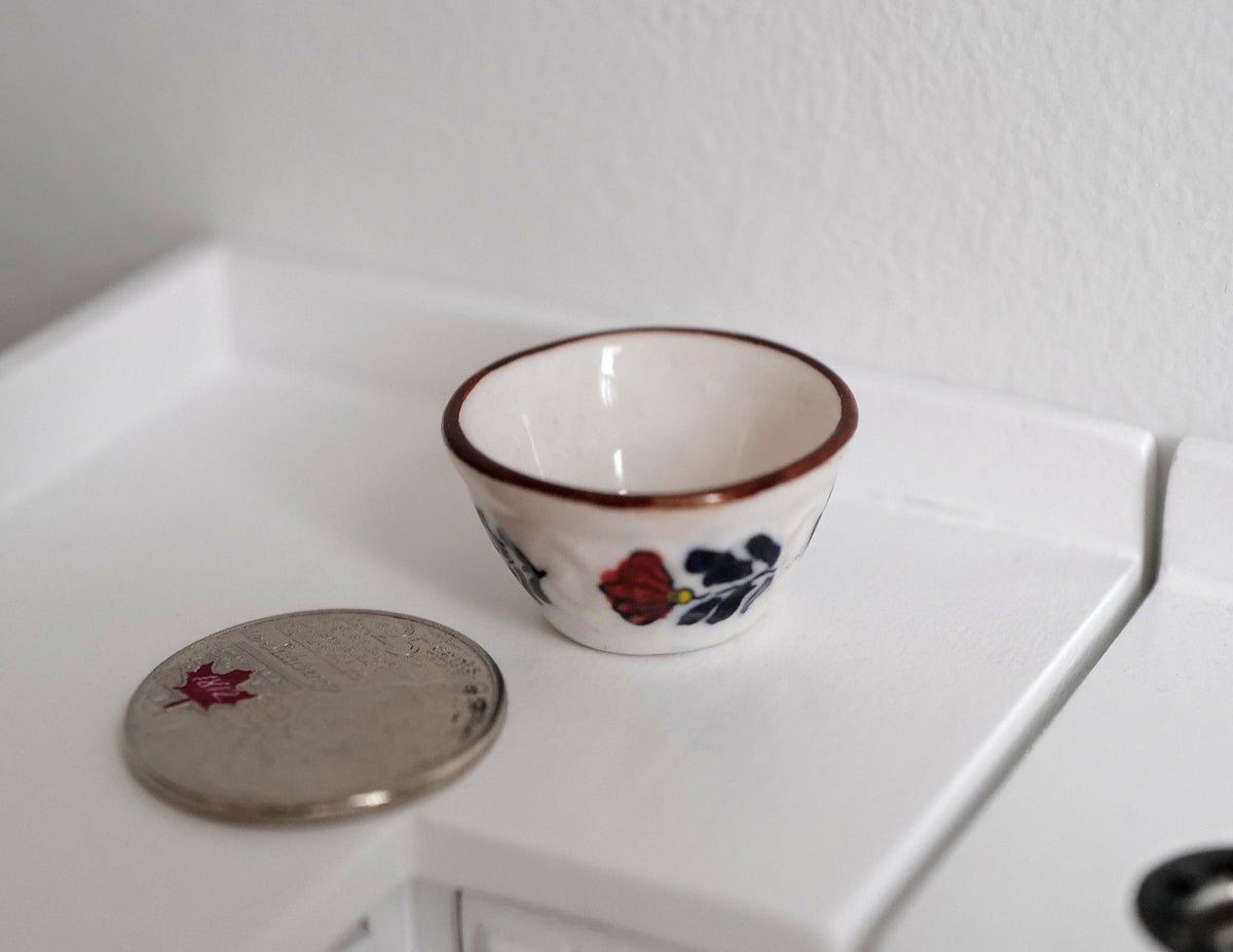 1:12 scale miniature ceramic bowl with fruit pattern and red rim on white, on a counter beside a coin for scale