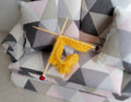 1:12 scale miniature wood knitting needles with yellow yarn and knitted piece, red tips, shown on a patterned sofa