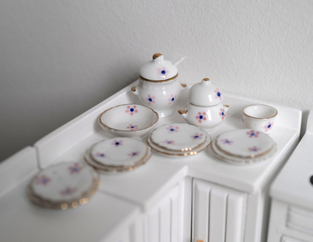 1:12 scale miniature white porcelain dinner set with pink floral pattern and gold rims, set of 12, on a counter